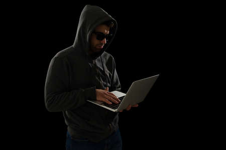 Dangerous criminal with black sunglasses typing on the laptop and scamming people onlineの写真素材