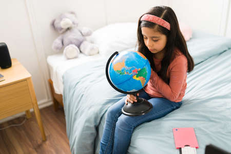 Wanderlust. Cute elementary girl sitting in her bed and learning the names of the countries on a...