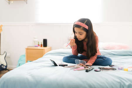 Adorable girl dreaming of becoming a makeup artist while playing with beauty products in her bedの写真素材