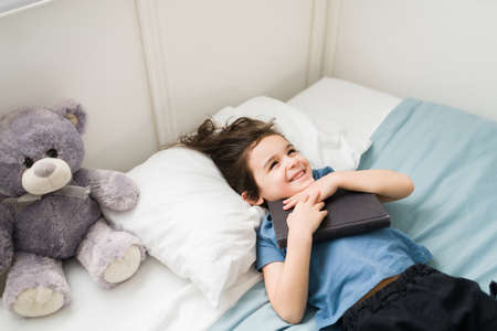 I love fairy tales. Smart little child lying in bed with a book after reading and feeling happy