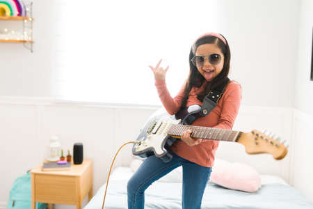 Playful little girl making the rock and roll sign and sticking her tongue out while playing the electric guitarの写真素材