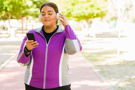 I enjoy listening to music while exercising. Happy obese woman using wireless headphones and her...