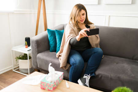 Attractive woman in her 30s suffering from a sore throat and speaking with a virtual doctor on a...