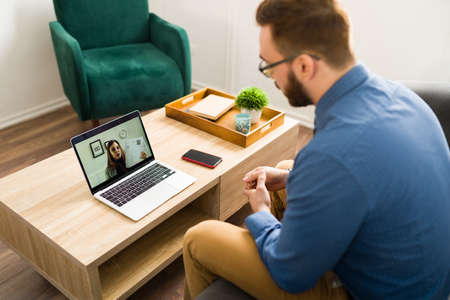 Looking for a new job. Professional caucasian man seen from behind speaking with a recruiter during a virtual interview on a video callの写真素材