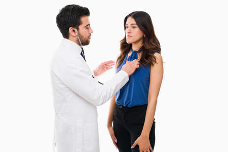 Hispanic woman getting a medical check up with a professional doctor. Physician using the stethoscope and listening to a patient's heartの写真素材