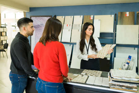 Attractive salesperson at the floor shop showing a couple of clients some beautiful tiles for their kitchenの写真素材