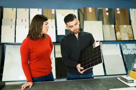 Caucasian young woman and latin man choosing new tile floors for their house at the furniture storeの写真素材