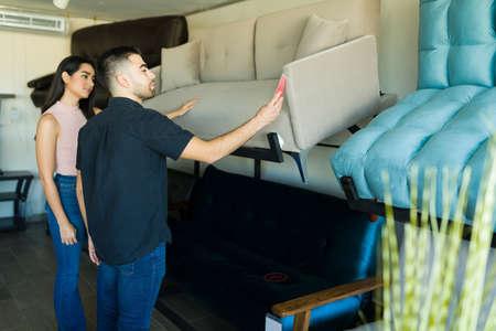 Handsome latin man and woman buying a new sofa for their house. Couple looking at the sale prices at the furniture storeの写真素材