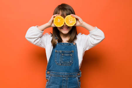 Pretty little girl having fun with fruit and holding two halves of oranges in front of her eyesの写真素材