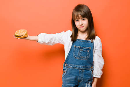 Caucasian little girl holding away a hamburger and looking displeased because fast food is not the best choice for your healthの写真素材