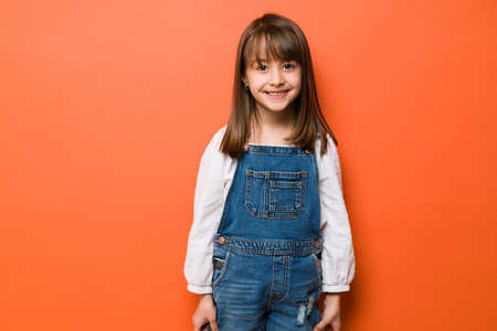 Beautiful brunette little girl smiling in a studio against an orange backgroundの写真素材
