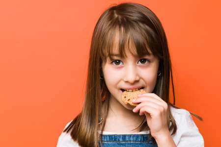Closeup of a beautiful little girl biting a chocolate chip cookie in a studioの写真素材