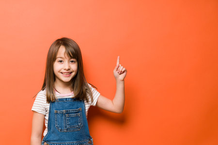 Happy Caucasian girl pointing up towards copy space while dressed casually in a studioの写真素材