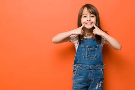 Portrait of a pretty little girl with a big smile pointing at it with her fingers with plenty of...