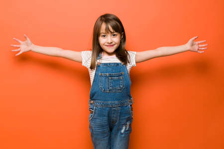 Beautiful little Caucasian girl with arms wide open and ready to give a big hug with a smile in a studioの写真素材