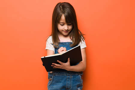 Cute little brunette taking some notes and writing on a personal diary in a studio
