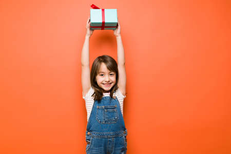 Beautiful little Caucasian girl lifting a birthday present over her head with a smile in a studio