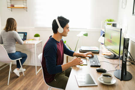 Centennial young man and designer working from home with his girlfriend. Designer with headphones...