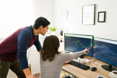 Checking the stock market. Gen z brokers investing and selling cryptocurrency while pointing at the computer screenの写真素材