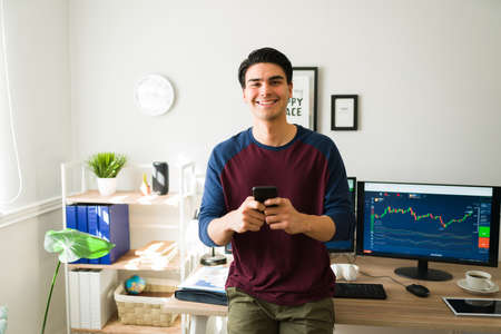 Portrait of an attractive hispanic man and broker smiling while texting clients about stock trading...