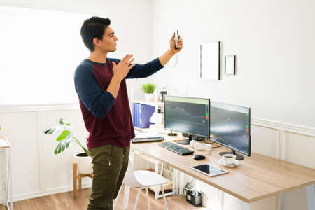 Handsome man recording himself on the smartphone. Broker live streaming while talking about cryptocurrencyの写真素材