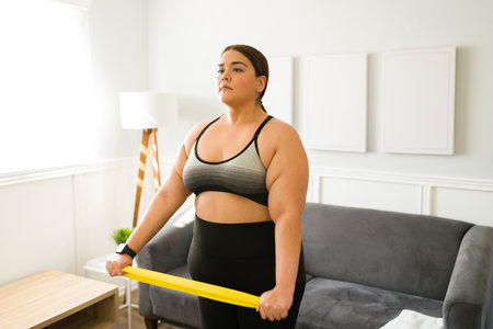Attractive latin woman working out with a resistance band during cardio exercises at homeの写真素材