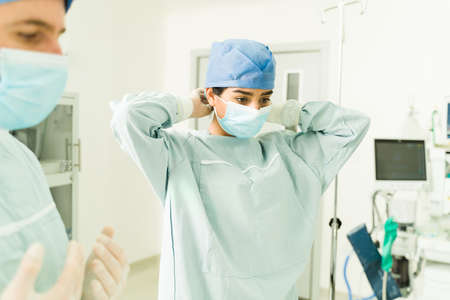 Beautiful surgeon with a face mask putting on scrubs to perform a difficult surgery at the operating...