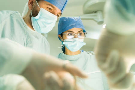Emergency surgery. Close up of two successful surgeons performing a surgery with a medical staff
