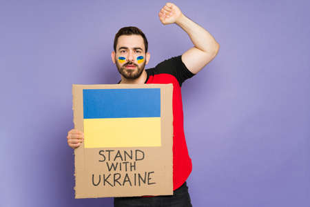 Man with a beard raising his arm and holding a placard in support for Ukraine during the warの写真素材