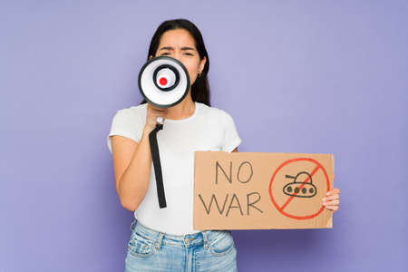 Hispanic woman holding a megaphone and a placard and protesting against war in a studio