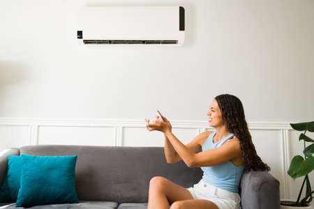Frustrated young woman feeling worried about her broken air conditioner and remote control