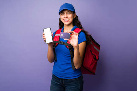 Portrait of a female delivery person showing her smartphone screen and a credit card while delivering foodの写真素材