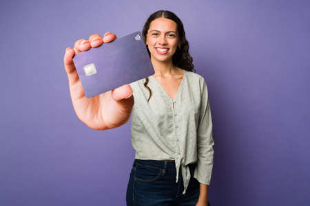 Portrait of an attractive young woman showing a big purple credit card in front of a studio...