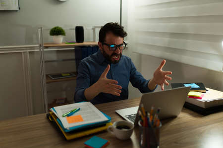 Stressed angry man screaming at the computer and looking furious because of a work mistake