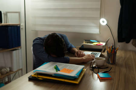 Overworked man taking a nap at his office desk while staying during the night to work on a deadline