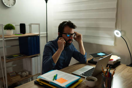 Workaholic man using a headset to make work calls during the night while working from home