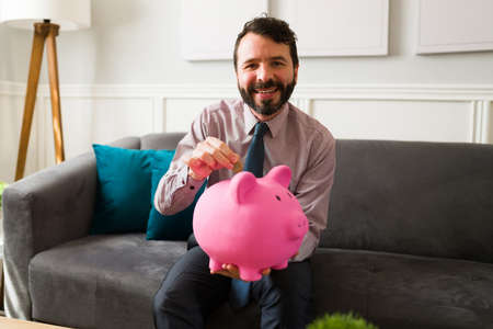 Financial freedom concept. Handsome wealthy man with a lot of money using a piggy bank for his...