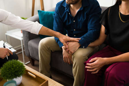 Close up of a therapist holding the hands of a couple to give them comfort while giving advice for their marriage problemsの写真素材