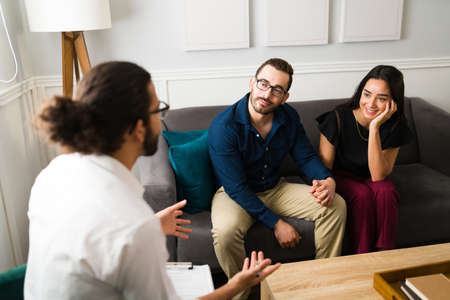 Cheerful couple smiling and solving their marriage problems while listening to the therapist's...