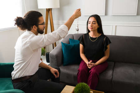 Male hispanic therapist trying an hypnosis tecnique to treat a patient with her depression and anxietyの写真素材