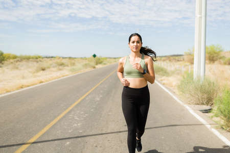 Fitness young woman wearing sportswear running in a deserted road during a sunny dayの写真素材