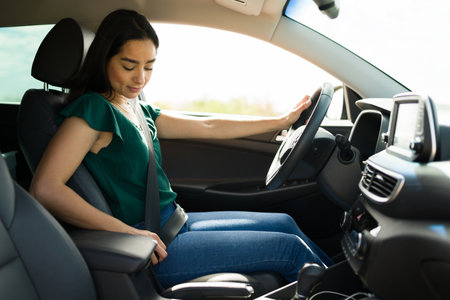 Female young driver putting on her seat belt while getting in the car to start working on a ride share appの写真素材