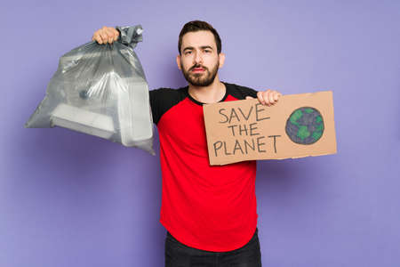 Distressed man holding a bag of trash and protesting against pollution and plastic. Young man trying to save the planetの写真素材
