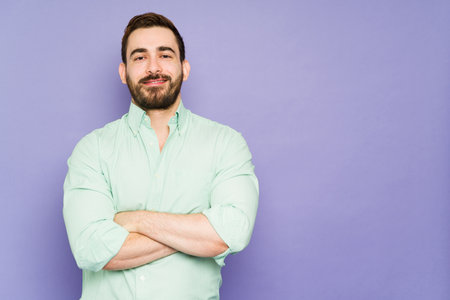 Confident attractive man with his arms crossed smiling while standing in front of a background with...