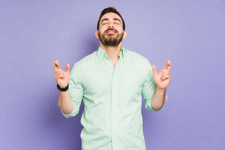 Attractive man feeling lucky and crossing his fingers hoping for his dreams to come true