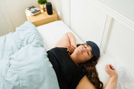 Top view of a relaxed overweight woman with a mask lying in bed under the covers after a good night sleepの写真素材