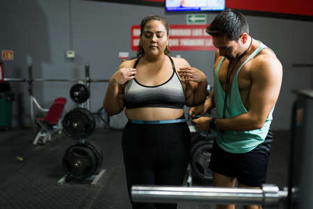 Weight loss concept. Personal trainer measuring the abdomen of an overweight young woman to start a fitness workoutの写真素材