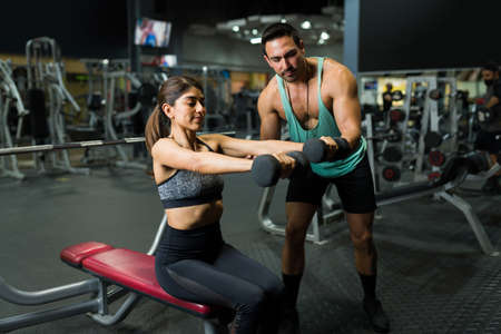 Fit young woman lifting weights with the help of a male personal trainer. Strong fitness coach working with an active womanの写真素材