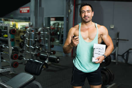 Happy young man and personal trainer holding a clipboard and a timer to start a fitness workoutの写真素材