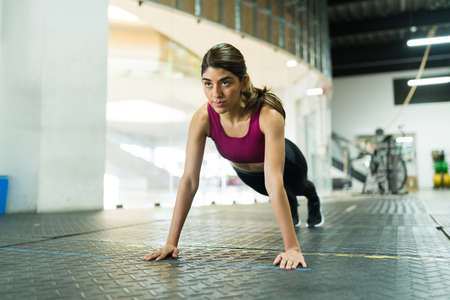 Attractive hispanic woman doing a plank at the gym. Beautiful fit woman exercising and doing push upsの写真素材